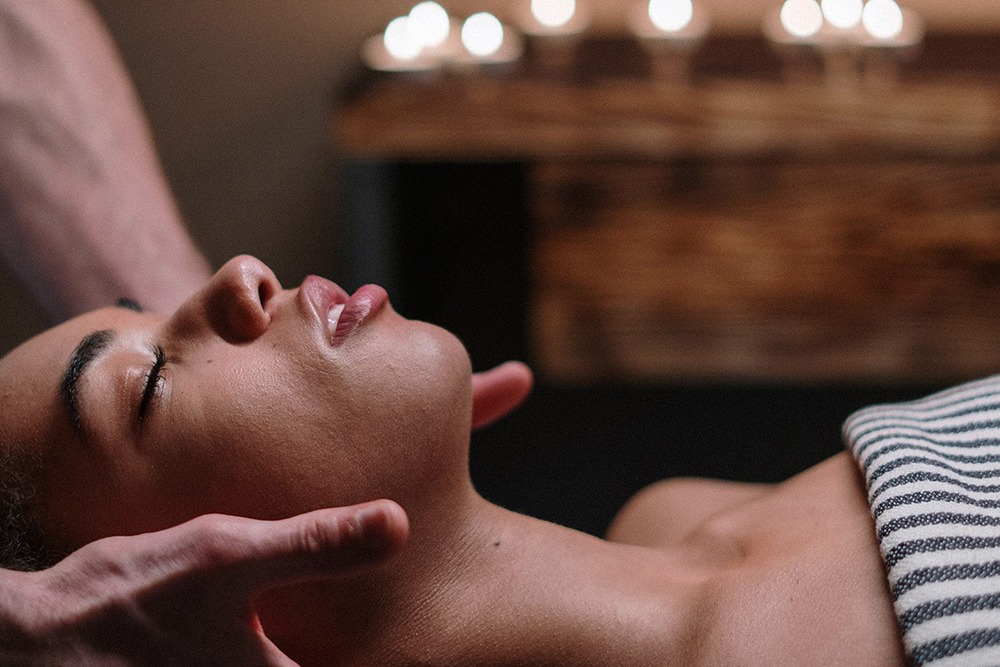 Person receiving a relaxing facial massage in a peaceful, candle-lit environment